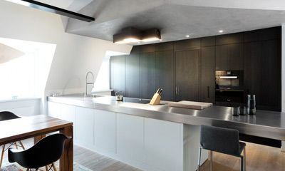 Moderne Küche mit dunklen Einbauschränken, Edelstahl-Arbeitsplatte, Kochinsel, Messerblock und Einbauofen.